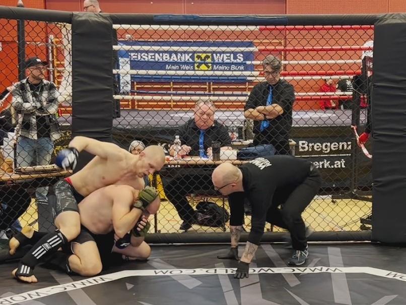 MMA-Käfig mit Sportlern und Offiziellen.